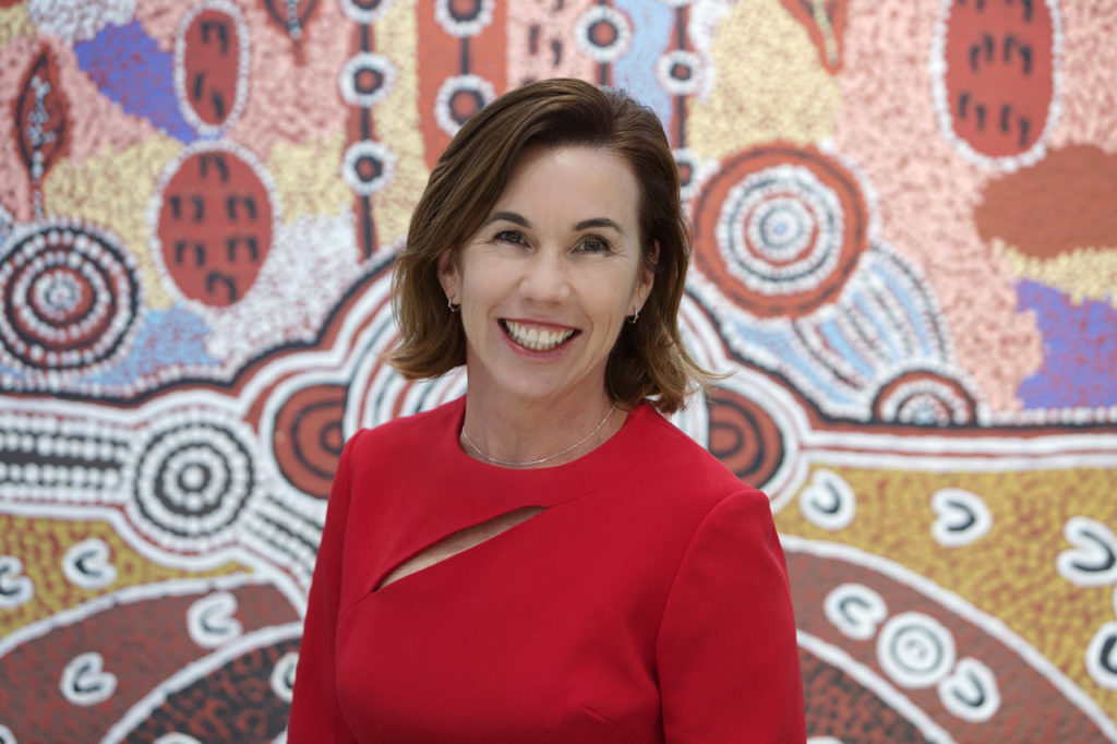 Uniting WA CEO, Amanda Hunt posing in front of Aboriginal reconciliation painting