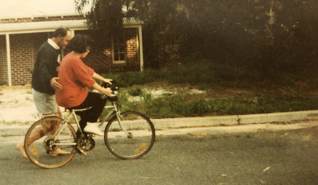 Jacinta riding a bike and being supported by her Dad