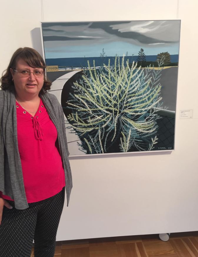 Kirsty standing next to one of her paintings in an exhibition