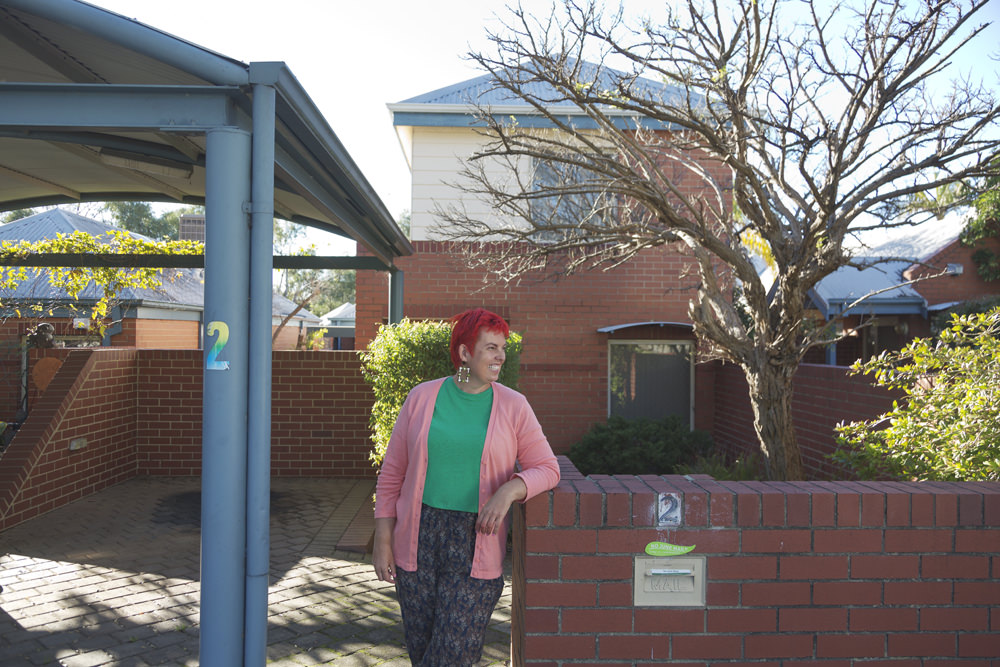 Person leaning on a brick wall out the font of their home with a tree in the background